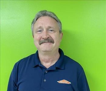 Male employee smiling with green wall background.